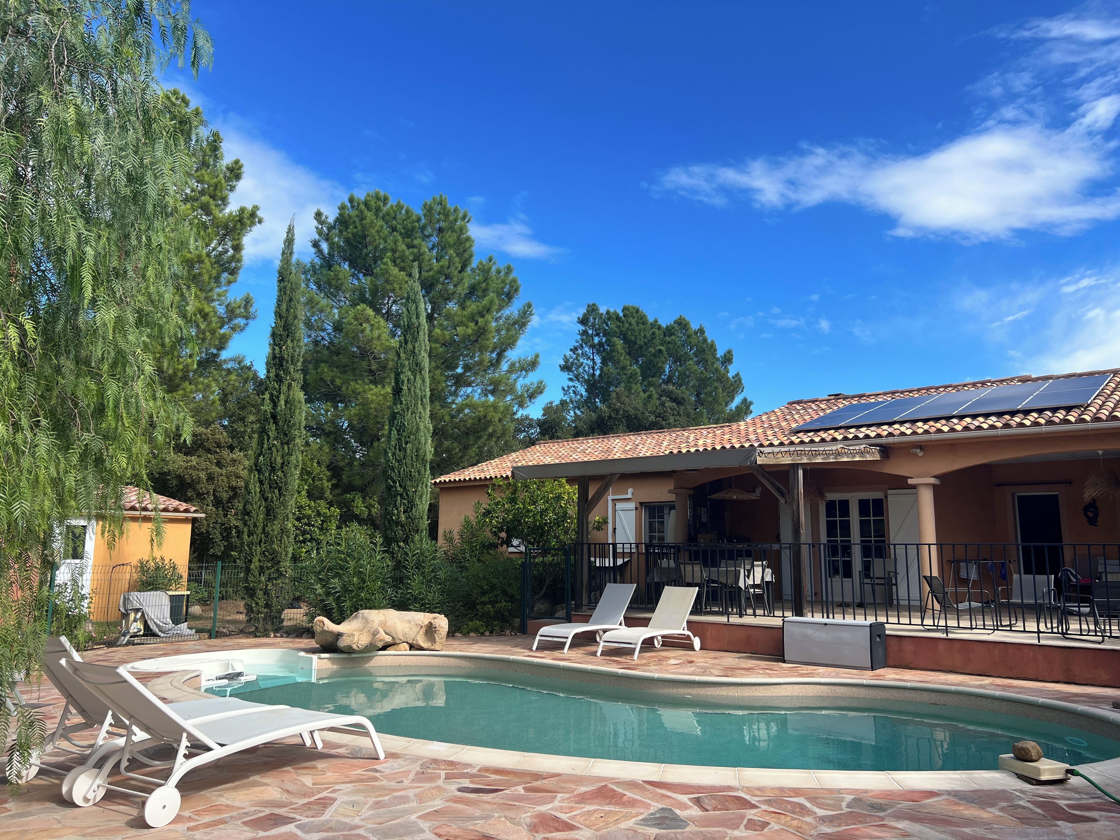 A swimming pool with lounge chairs, a covered patio, and a building with solar panels.