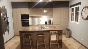 Een moderne keuken met roestvrijstalen apparatuur, een centraal eiland met krukken en een wandklok.
