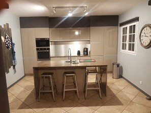 Eine moderne Küche mit Edelstahlgeräten, einer zentralen Kochinsel mit Hockern und einer an der Wand befestigten Uhr.