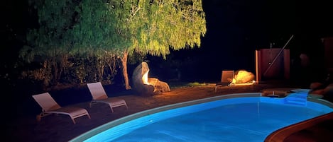 En swimmingpool med solstolar och ett träd som är upplyst med artificiell belysning.