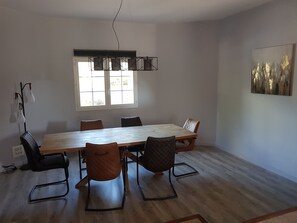 A dining area with a wooden table, six chairs, a hanging light fixture, a window, and a painting on the wall. - 150 m² air-conditioned detached villa near Porto Vecchio (San-Gavino-di-Carbini)