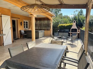 Une terrasse extérieure avec une table et des chaises, un barbecue et un espace salon abrité.