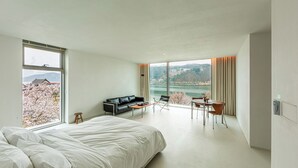 Ett modernt hotellrum med en stor säng, en soffa, ett matbord och utsikt över en sjö och berg.