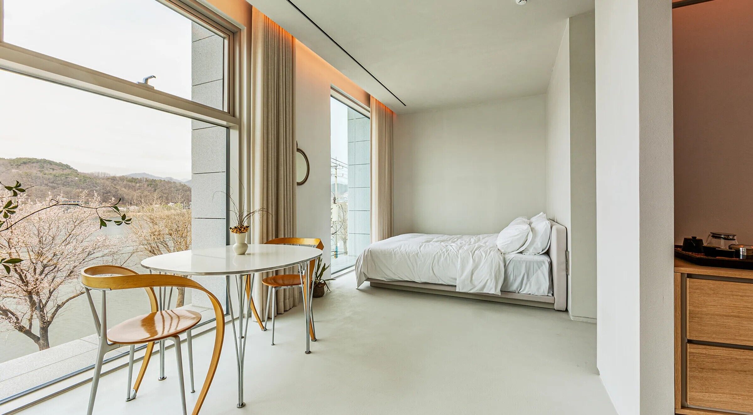 A modern bedroom with a bed, a dining table with chairs, and a view of the outdoors.
