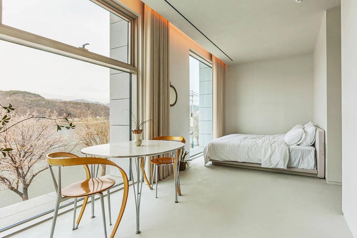 A modern bedroom with a bed, a dining table with chairs, and a view of the outdoors.