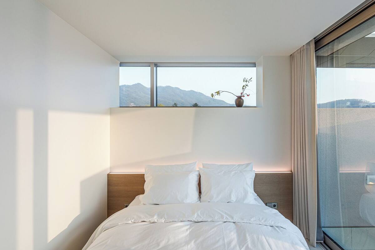 A modern hotel room with a large bed, a nightstand, a window with a view of mountains, and a vase with flowers.