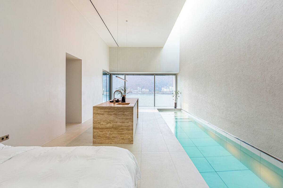 A modern hotel room with a large bed, a small wooden side table, a bathroom with a glass-enclosed shower, and a view of a cityscape.