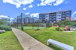 Ein Wohnkomplex mit Sportbereich, darunter ein Fußballfeld und ein Spielplatz, umgeben von Grünflächen und blauem Himmel.
