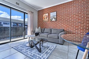 Ein modernes Wohnzimmer mit einem grauen Sofa, einem Glastisch und einer Ziegelwand.