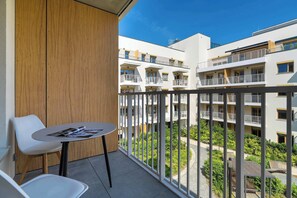 Ein Balkon mit Tisch und Stühlen, eine Holzwand und Blick auf mehrstöckige Gebäude mit Balkonen.