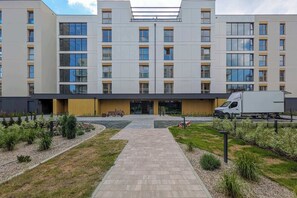 Ein modernes Mehrstöckengebäude mit einem zentralen Eingang und einem gepflasterten Weg dorthin.