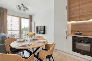 Eine moderne Küche mit Einbauofen, ein Essbereich mit rundem Tisch und Stühlen und Blick auf ein Gebäude durch große Fenster.