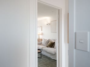 Une porte qui donne sur un salon, où se trouvent un canapé, une lampe et un tableau encadré au mur.