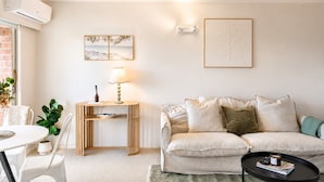 A modern living room with a sofa, a dining table, and a lamp. - Walk to Beach | Sky Tower & Ocean Sunset Views | ✨Sage & Sea by Homello✨ (Devonport)