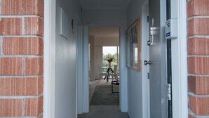 A hallway with a brick wall, white doors, and a view into a room with a table and chairs. - Walk to Beach | Sky Tower & Ocean Sunset Views | ✨Sage & Sea by Homello✨ (Devonport)
