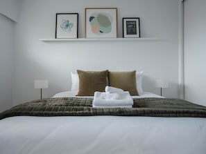 Une chambre d’hôtel avec un lit bien fait, deux oreillers, une couverture et trois œuvres d’art encadrées accrochées au mur.