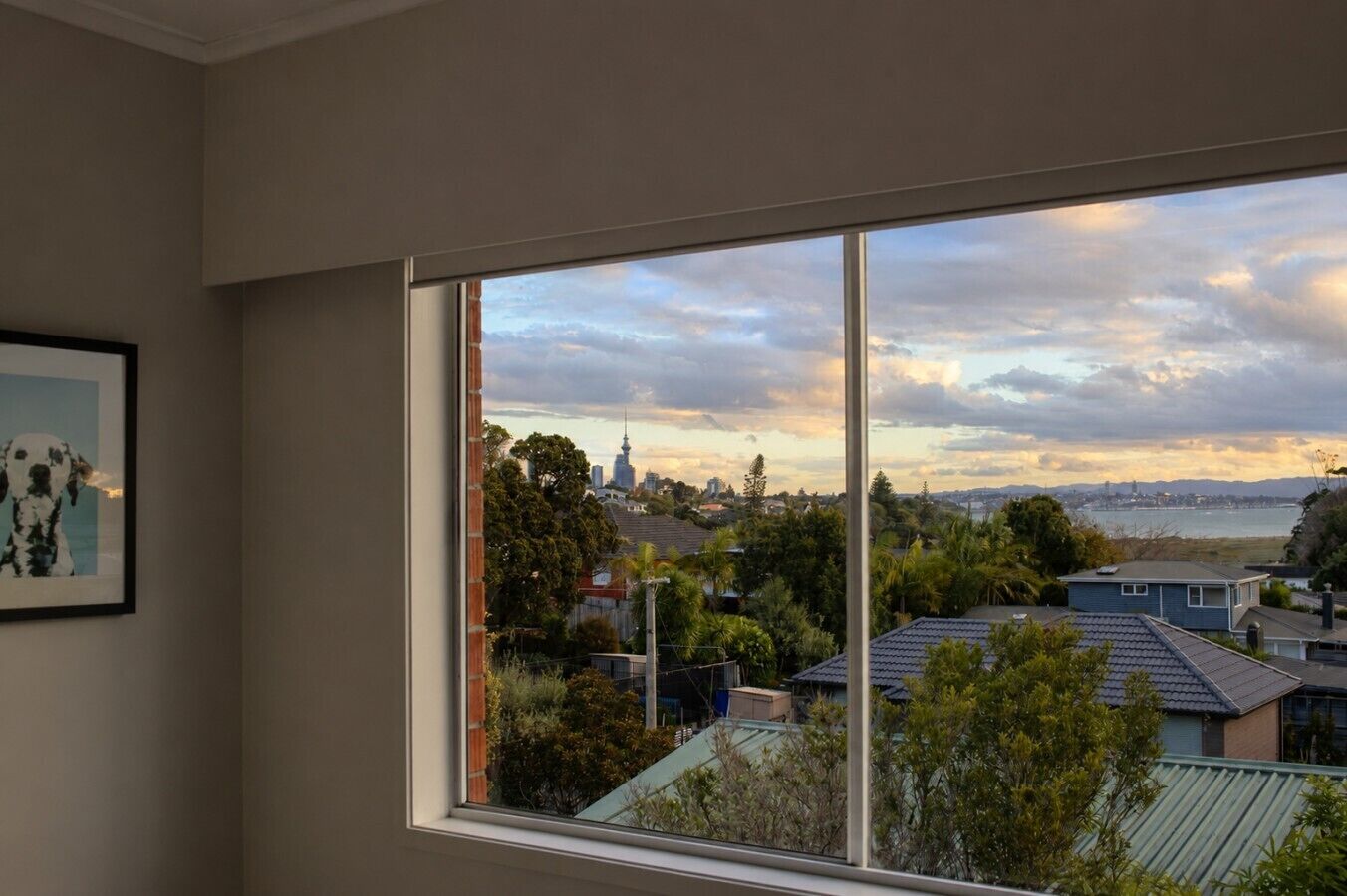 Quarto com uma grande janela com vista para a paisagem urbana, um quadro na parede e vislumbre do céu.
