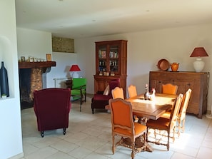 Une salle à manger avec une table en bois, des chaises, une cheminée, une bibliothèque et une lampe.