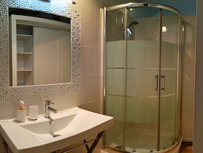 Ein Badezimmer mit einem weißen Waschbecken, einem Spiegel, einer Duschkabine aus Glas und einer strukturierten Wand.