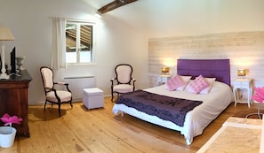 Une chambre à coucher avec un lit, deux chaises, une table de chevet, une lampe, un radiateur et une fenêtre.