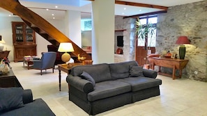 Ein geräumiger Wohnbereich mit grauem Sofa, Holzmöbeln, einer Treppe und Stegwänden.