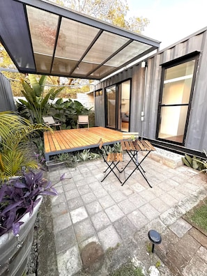 Eine moderne Terrassenausstattung mit Holztisch und -stühlen, einer Pergola und Kübelpflanzen.