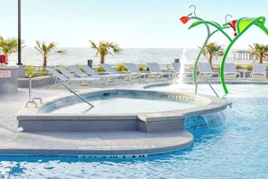 Ein Swimmingpool mit Liegestühlen, einem Wasserspiel und Blick auf das Meer.