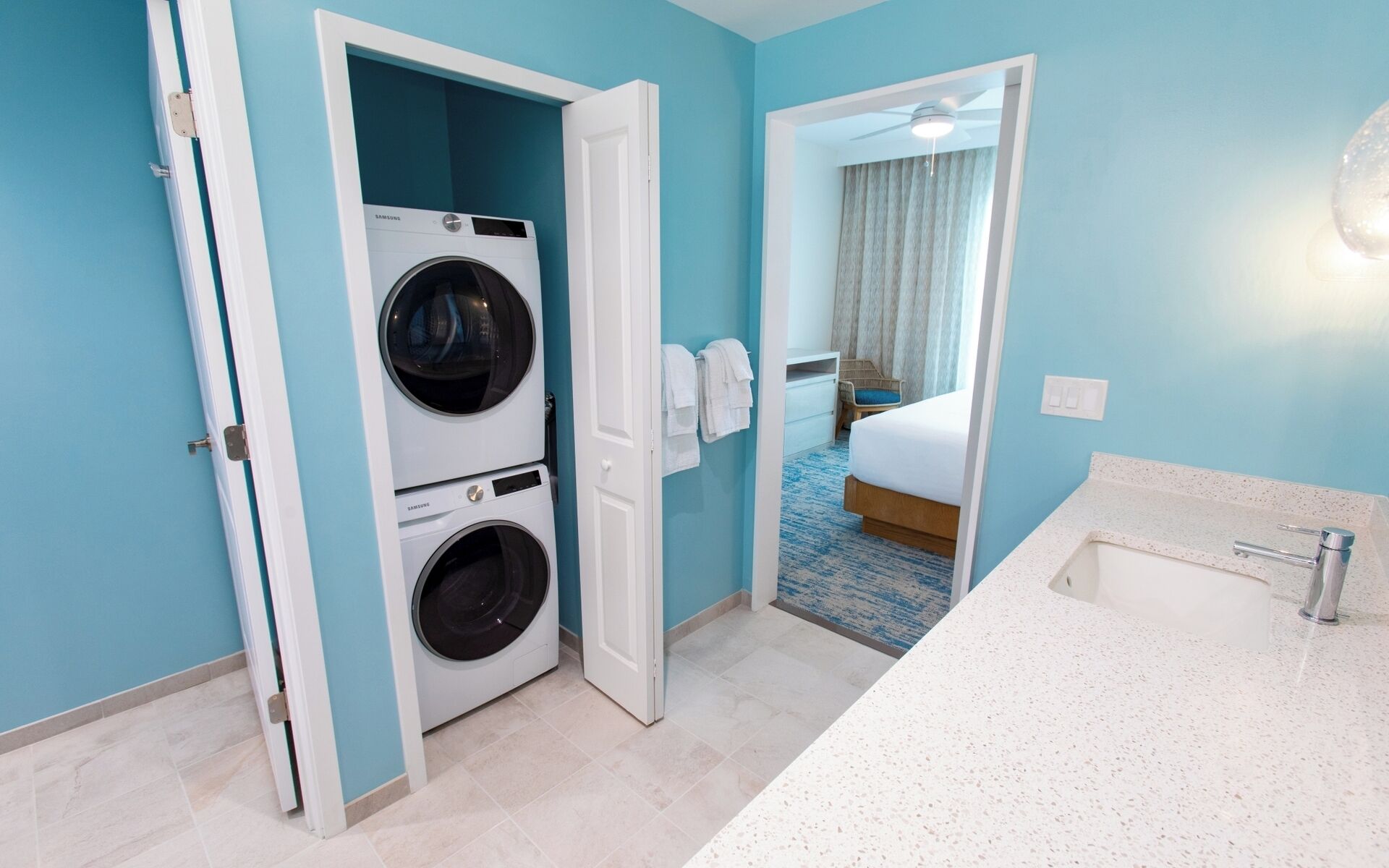 Hotelkamer met een wasmachine, een bed, een badkamer met een wastafel en een spiegel.