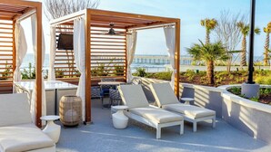 Un salón en la azotea con pérgolas de madera, sillones blancos acolchados, una mesita y un ventilador de techo.