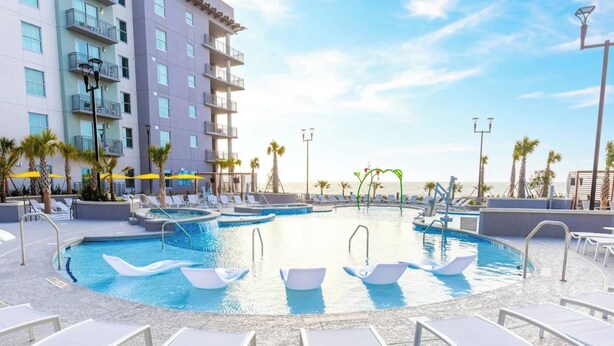 Un área de piscina con varias piscinas, sillas de descanso y un edificio con balcones.