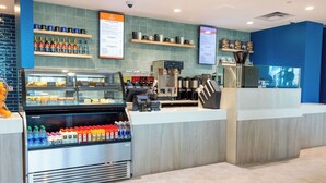 Un café moderno con una estación de autoservicio para bebidas, una máquina de café y un panel de menú.