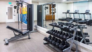 Uma academia com equipamentos de musculação, esteiras e um espelho grande na parede.