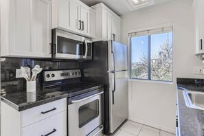 Eine moderne Küche mit weißen Schränken, Edelstahlgeräten, einem großen Fenster und Blick auf Bäume.