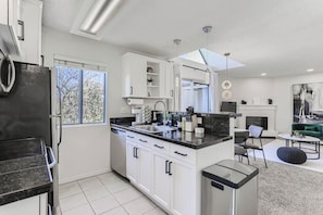 A modern kitchen with white cabinets, a black countertop, and a built-in dishwasher. - Bright DTC 2BR Condo with Pool & Fireplace (Greenwood Village)
