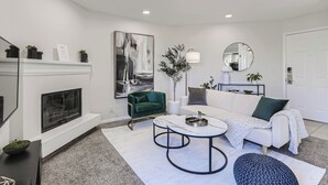Een moderne woonkamer met een open haard, een groene fauteuil, een witte bank en een ronde salontafel.