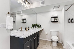 A modern bathroom with a double sink vanity, a toilet, a shower area, and a large mirror. - Bright DTC 2BR Condo with Pool & Fireplace (Greenwood Village)