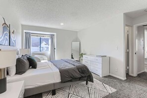 A modern bedroom with a bed, bedside table, dresser, and a window with curtains.