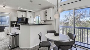 Een moderne keuken met witte kasten, een centraal eiland en een eethoek met stoelen.