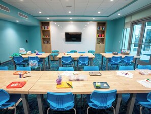 Une salle de conférence avec des chaises bleues, des tables en bois, un écran de télévision et des armoires de rangement.