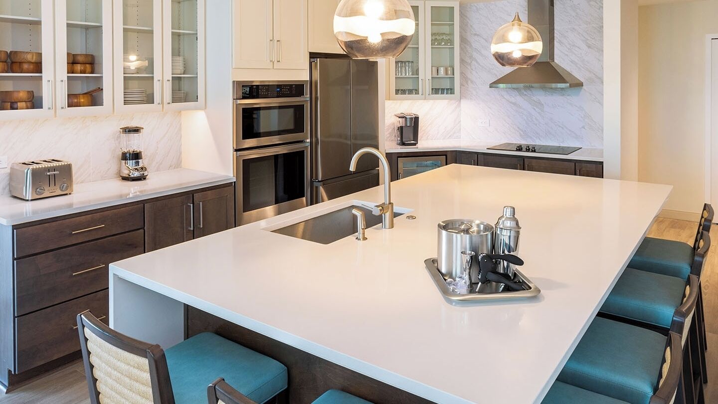 A modern kitchen with a central island, stainless steel appliances, and a seating area with blue chairs.