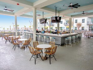 Un espace bar extérieur avec des tables et des chaises, un comptoir et des ventilateurs de plafond.