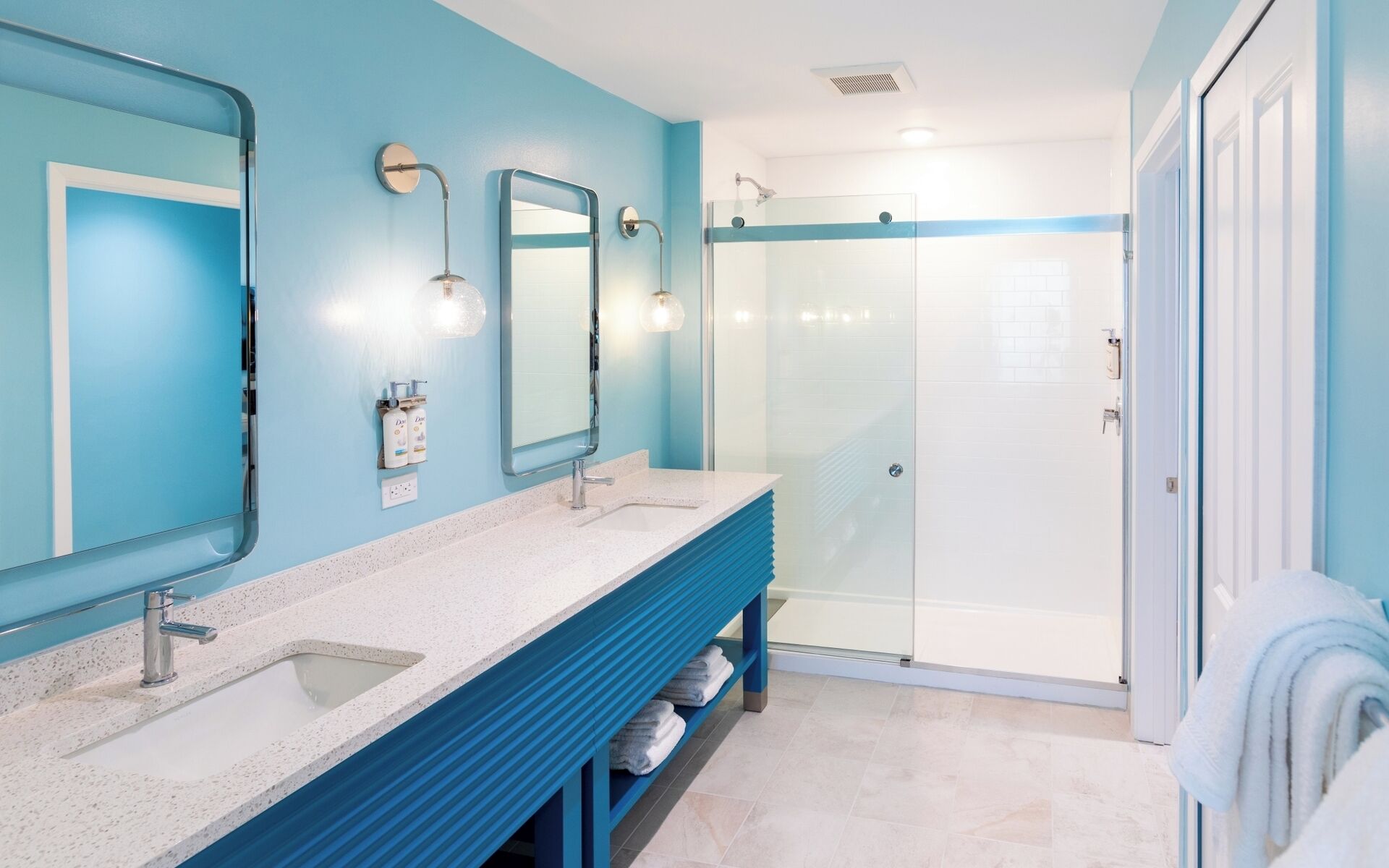Un bagno con due lavandini, uno specchio, una doccia e un portascopevoli.