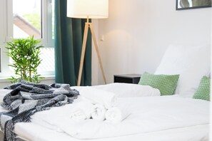 A neatly made bed with rolled towels, a green plant, and a lamp beside it. - In the middle of the wine region & Black Forest: Stylish apartment (Oberkirch)