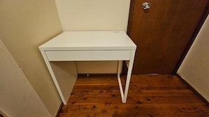 A white desk in a corner with a wooden floor and a door in the background.