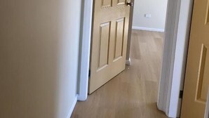 Un couloir avec une porte en bois, des moulures blanches et un plancher de couleur claire.
