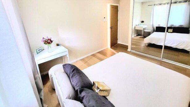 Une chambre d’hôtel avec un lit, une table de chevet ornée d’un vase de fleurs, un miroir et une porte donnant sur une autre pièce.