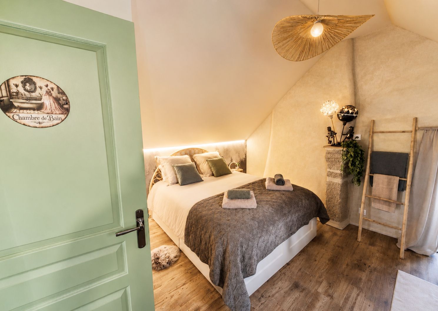 A bedroom with a bed, pillows, a bedside table, a lamp, and a door with a sign.