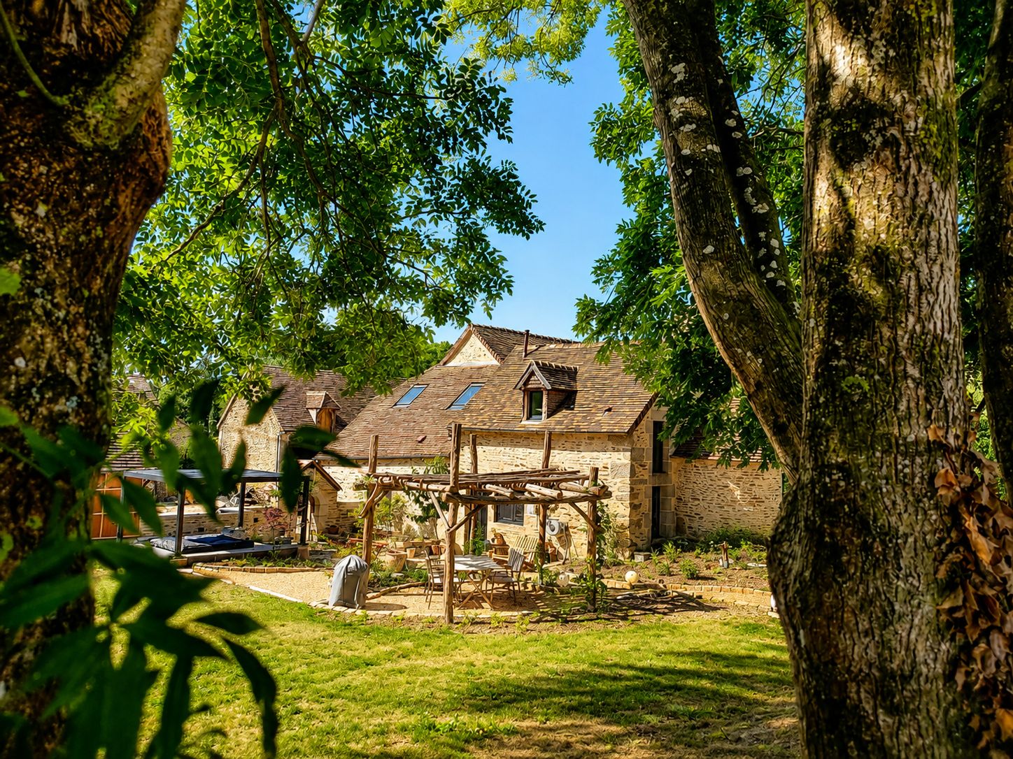 Un bâtiment rustique en pierre, doté d’un toit en pente, entouré d’arbres et d’une pelouse bien entretenue.