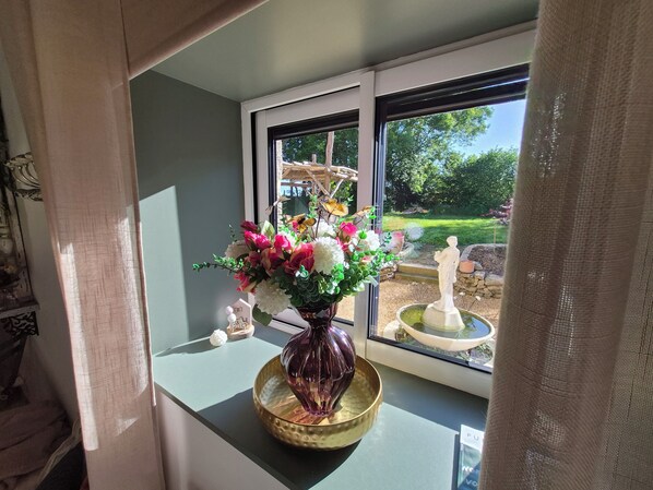 A window with a vase of flowers, a statue, and a garden view.