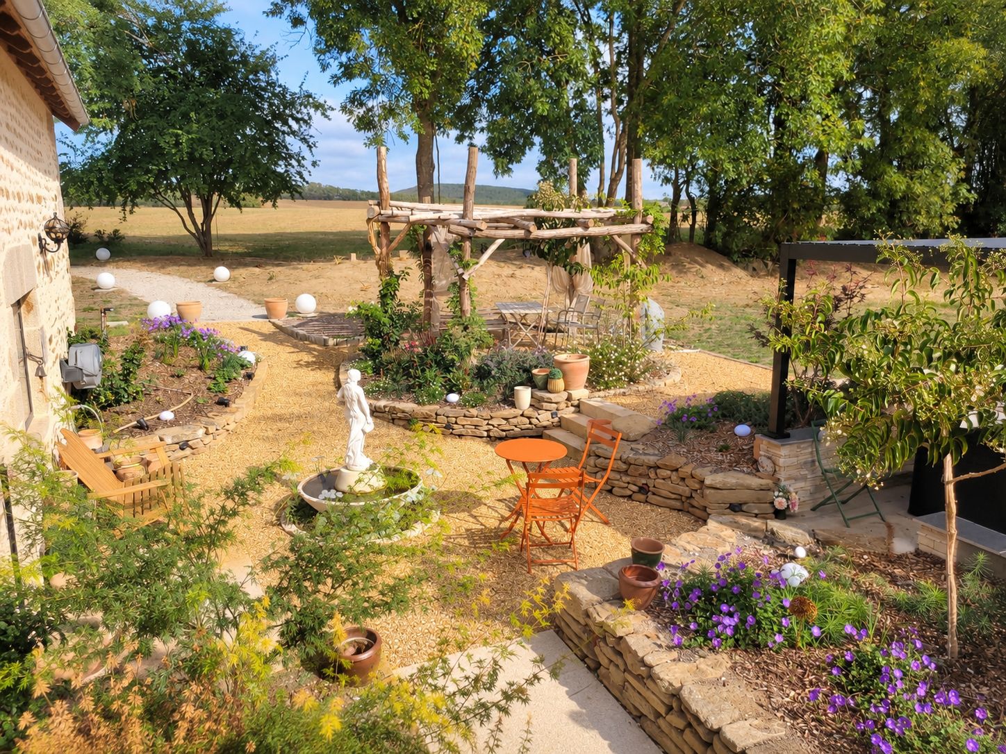 Ein Garten mit einer Pergola, Sitzgelegenheiten im Freien und verschiedenen Pflanzen und Blumen.